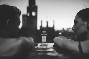 Two people in a pool between a bottle of fragrance