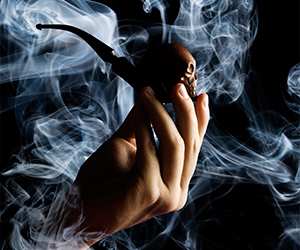 Hand holding a pipe and shrouded in smoke