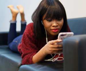 A woman relaxing on a couch with her phone and headphones put on
