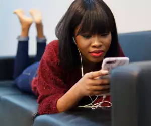 A woman relaxing on a couch with her phone and headphones put on